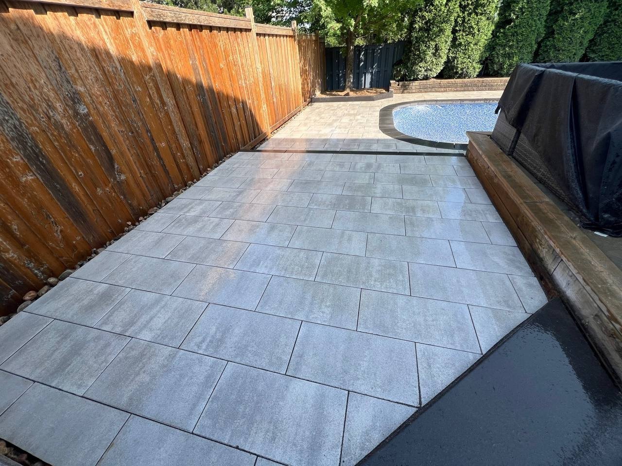 Modern outdoor kitchen featuring pergola, grill, and bar seating in backyard Completed backyard pool landscaping and interlocking patio
